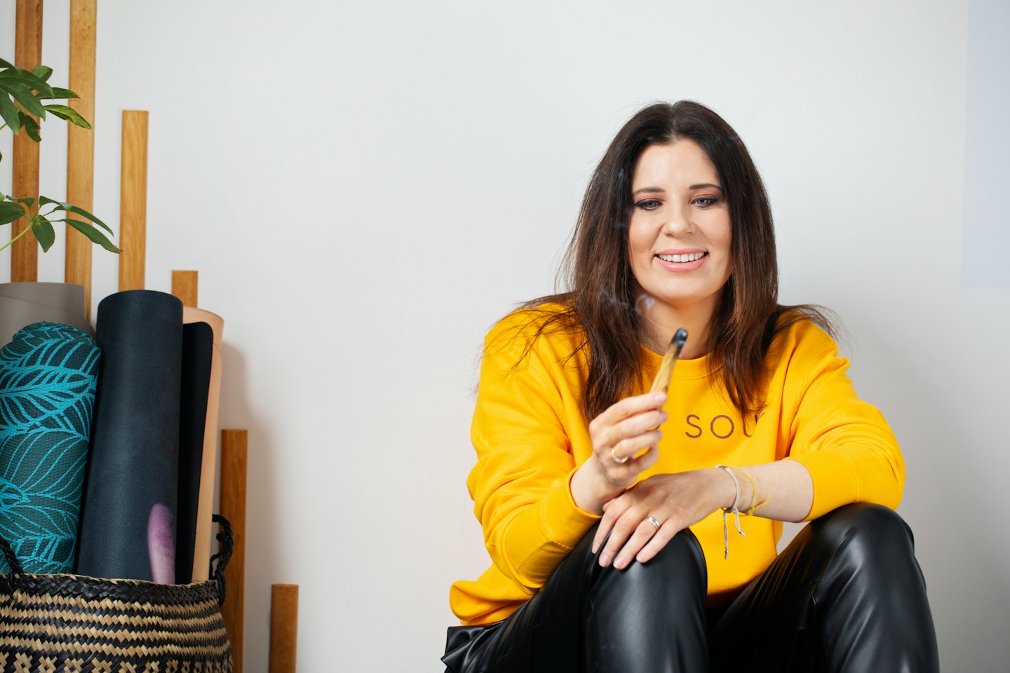 Woman in a yellow sweatshirt holding a smoking palo santo stick.